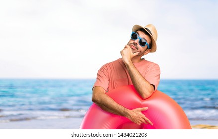 Man with hat and sunglasses on his summer vacation standing and thinking an idea at the beach - Powered by Shutterstock