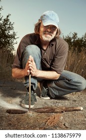 Man in hat trying to make a fire with wood stick friction