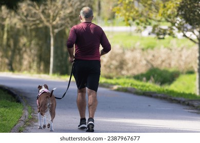 A man have jogging in park with dog on a leash