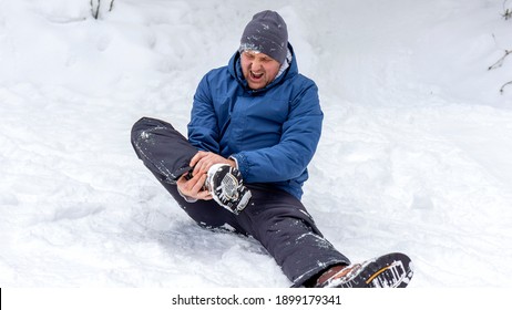 Man having ankle injury while having outdoor activities in cold weather condition. Male climber lying on the snow and touching his injured leg. Young man suffering from pain in leg. Healthcare concept
