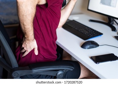 Man having back pain while working from home in an improvised office in the living room