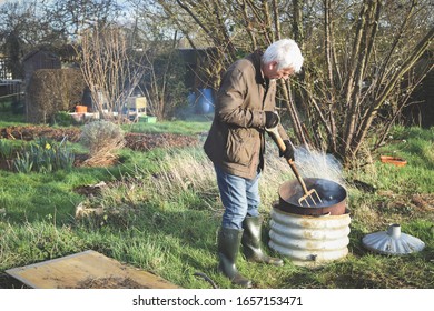 Man having a bonfire at an allotment or community garden vegetable plot to dispose of garden waste - Powered by Shutterstock