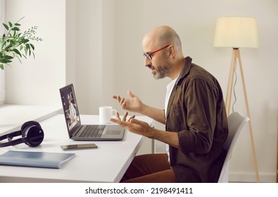 Man Having Casual Online Business Meeting At Home. Side View Of Man In Glasses Sitting In Front Of Modern Laptop Computer In His Homeoffice, Gesturing And Discussing Work With Colleague On Videocall