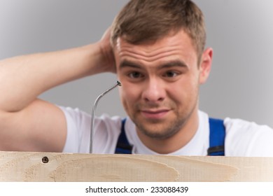 Man having difficulty getting nail hammered into wood. guy thinking and looking at bent nail on grey background 