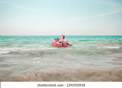 A Man Is Having Fun On Pink Flamingo Inflatable Pool Float In The Turquoise Sea With White Waves