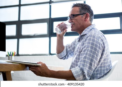 Man having glass of water and holding digital tablet in office