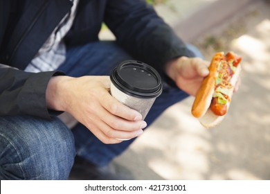 Man having lunch with hot dog and coffee in summer park, closeup outdoor photo with selective focus