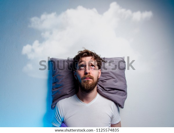 Man having\
problems/ insomnia, laying in bed on pillow, looking up to gray\
cloud over his head, copy space \
