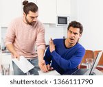 Man having problems with some documents; worriedly discussing with friend at home table