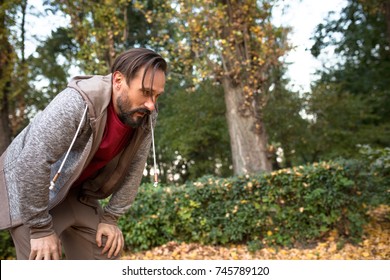 Man Having Short Rest To Take A Breath After Running In Urban Park. Adult Man Having Rest After Jogging.