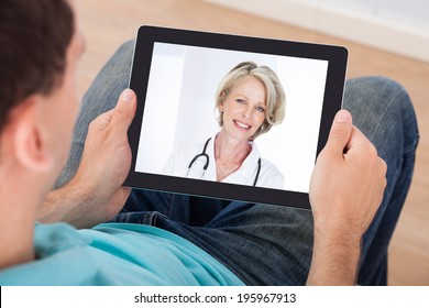 Man Having Video Chat With Female Doctor On Digital Tablet At Home