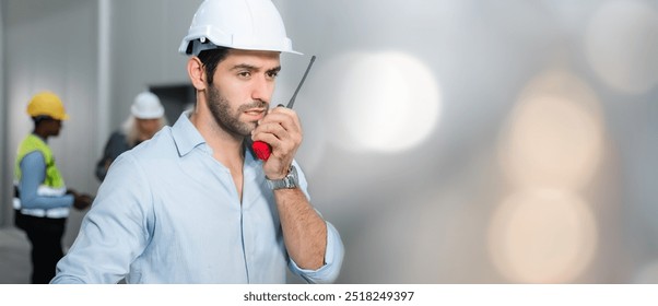 Man head engineer wearing white safety hardhat with walkie talkie inspecting construction site. Professional engineer work checking on factory floor - Powered by Shutterstock