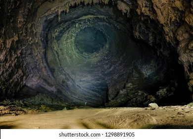 Man With Headlight Standing On A Rock Under A High Wall With Stalactites Inside The Giant Hang Tien Cave In The Phong Nha Ke National Park In Vietnam.