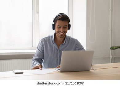 Man in headphones sit at desk with laptop working, take part in briefing on video call app. Millennial guy listens audio course or studying use modern tech. Virtual event, on-line counselling concept - Powered by Shutterstock