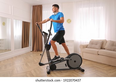 Man with headphones using modern elliptical machine at home - Powered by Shutterstock