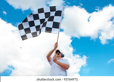 Man with headset holding and waving a checkered flag on a raceway
