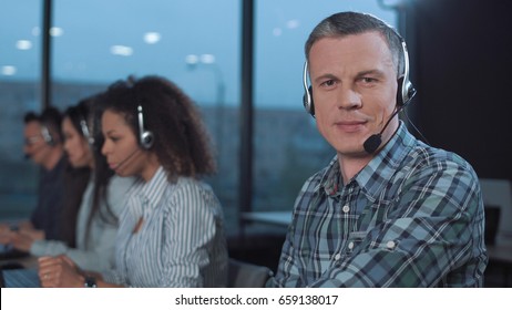 Man With Headset Working With Laptop And Looking At Camera.