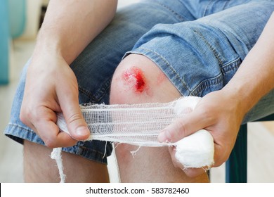 Man heals the wound on his knee at home. Holding the bandage at the hands 