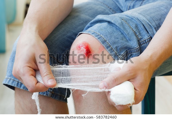 Man heals the wound on his knee at home. Holding\
the bandage at the hands 