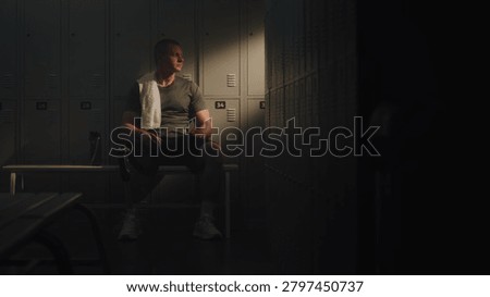 Man Heavily Sits Down on Bench, Leaning Back Against Metal Lockers For Support. Male Taking Deep, Labored Breaths Recover While Hydrating From Water Bottle. Grit, Determination of Resilient Athlete.