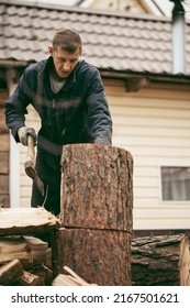 A man with a heavy axe in his hands. An axe in the hands of a lumberjack chopping or chopping tree trunks. A man is chopping firewood in the yard of a house in the village.