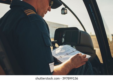 Man Helicopter Pilot Reading A Manual Booklet While Sitting In The Cockpit.