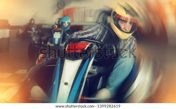 Man in helmet driving go-kart car in\
a circuit lap in sport club, people on\
background