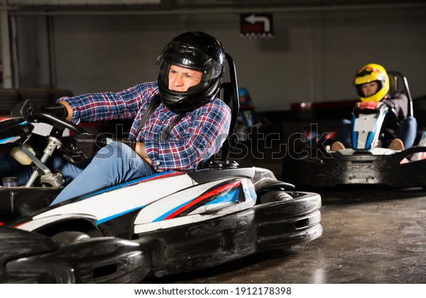 Man in helmet driving racing\
car for karting in a circuit lap in sport club, people on\
background