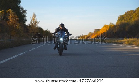 Man in helmet riding on a motorbike at autumnal highway. Motorcyclist driving his motorcycle on country road with headlights on. Freedom and travel concept. Slow motion Front view Close up.