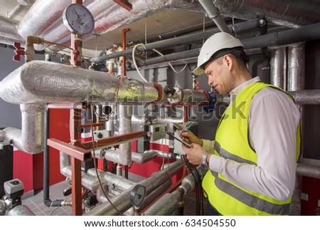 Man in helmet writing down measurements in boiler room