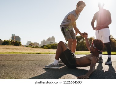 Man Helping Fallen Teammate To Stand Up. Man Extending Hand To Lift His Teammate Fallen On Ground.