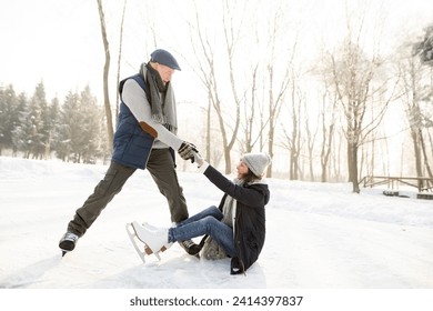 Man helping ice skating woman getting up from frozen lake - Powered by Shutterstock