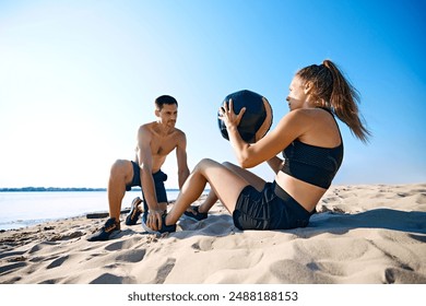 Man helping woman with hard press exercises with medicine ball on sandy beach under clear blue sky. Intensive workout. Concept of sport, active and healthy lifestyle, body care, fitness - Powered by Shutterstock