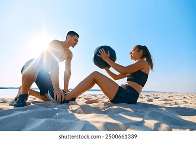 Man helping woman with hard press exercises with medicine ball on sandy beach under clear blue sky. Intensive workout. Concept of sport, active and healthy lifestyle, body care, fitness - Powered by Shutterstock