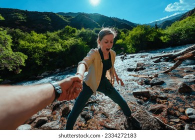 Man helps young woman hiker cross a mountain stream, first point of view - Powered by Shutterstock