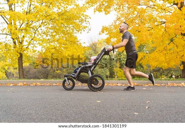 man with her daughter in jogging stroller outside\
in autumn nature
