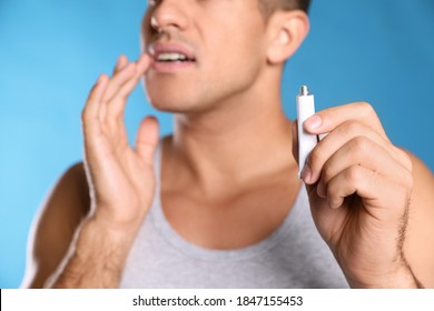 Man With Herpes Applying Cream On Lips Against Light Blue Background, Closeup