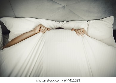 Man hiding in bed under sheets.