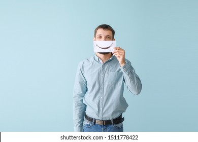 Man Hiding Mouth Behind Sheet Of Paper With Drawn Smile On Color Background