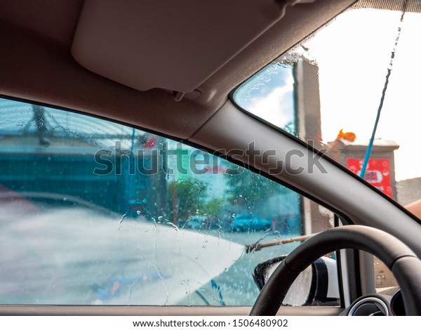 Man with the high powered hose in his hand washes\
his car at a self-serve car wash. View of water jet from the\
driver\'s seat.