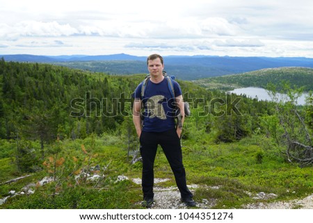 A man hiker with backpack standing on background of small mountains posing for picture.