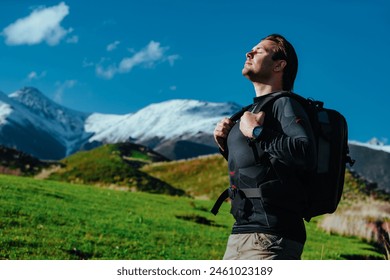 Man hiker with backpack stands in picturesque valley on mountains background with closed eyes - Powered by Shutterstock