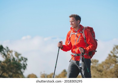 Man Hiker Hiking In Mountain Trail Path On Summer Outdoor Day Wearing Outerwear Jacket And Backpack For Camping. Guy Portrait Lifestyle Walking With Hiking Poles.