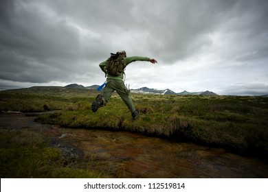 Man hiker jumping across small river - Powered by Shutterstock