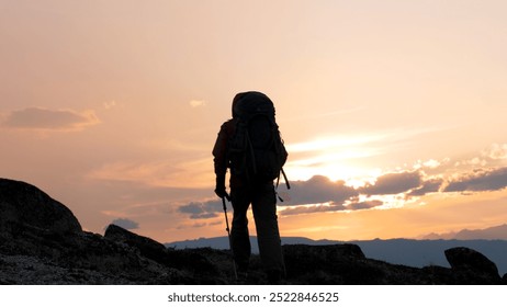 Man hiker porter climber with big backpack and trekking sticks poles raises up to top hilly cliff mountain. Walking at sunrise or sunset sky, sun rays shine. In trekking clothes for hiking. In motion - Powered by Shutterstock