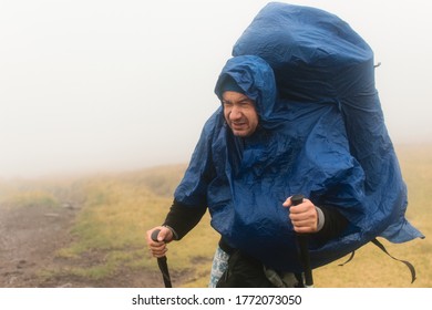 A Man Hiker In A Rain Cover In The Fog During Bad Weather.