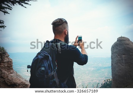 man hiker taking photo with smart-phone at mountain peak cliff