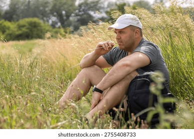 A man hiking with a backpack resting while sitting on the grass. Outdoor recreation.