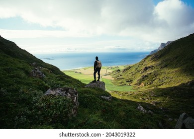 Man With Hiking Backpack Stand On Top Of Mountain, Overlook Epic Views And Nordic Scandinavian Landscape. Modern Adventure Traveller Concept. Young People Spend Quality Time In Nature