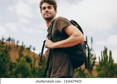 Man Hiking In A Countryside Location. Side View Of A Man Wearing A Bag Walking Through A Forest.